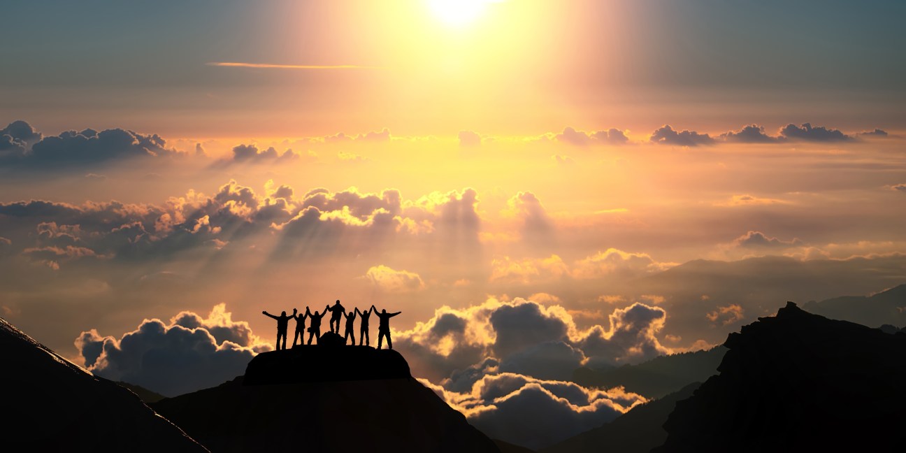 On the top of the world together. A group of people stands on a hill over the beautiful cloudscape.